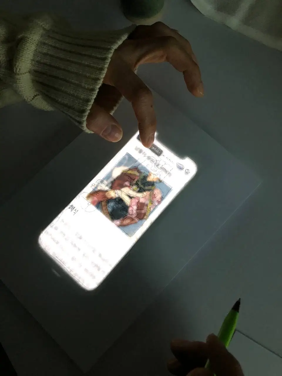 A hand tapping on a smartphone glowing from below a paper sheet